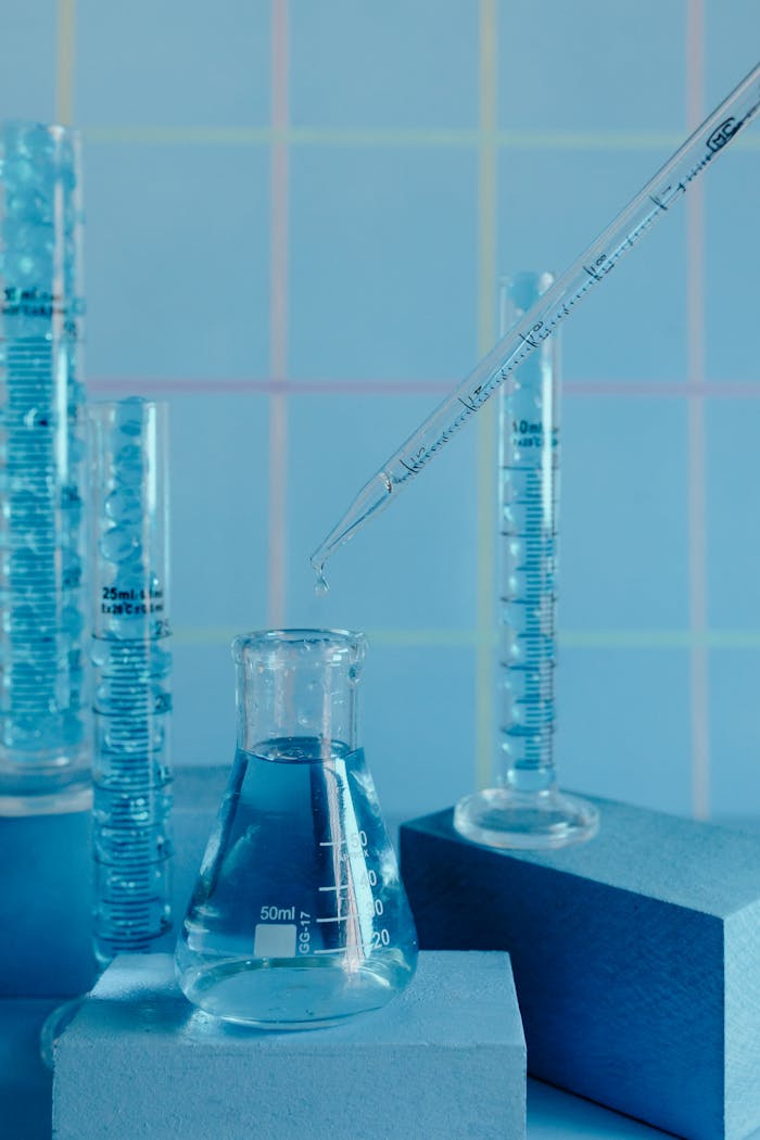 our-journey-01 Collection of blue-toned glassware in a laboratory setting with pipette and graduated cylinders.